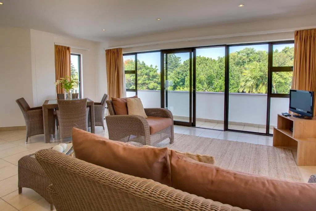 Living and dining area with wicker furniture opening onto a balcony over the treetops