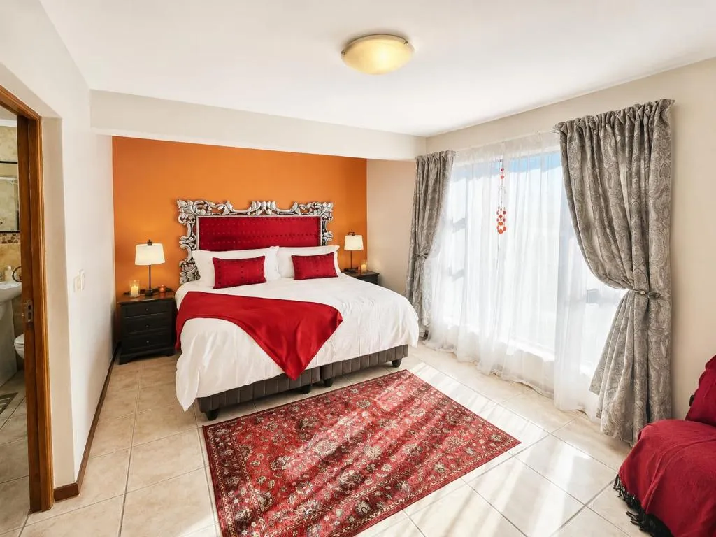 Bedroom with a red and orange accent wall, ornate headboard and sheer curtains