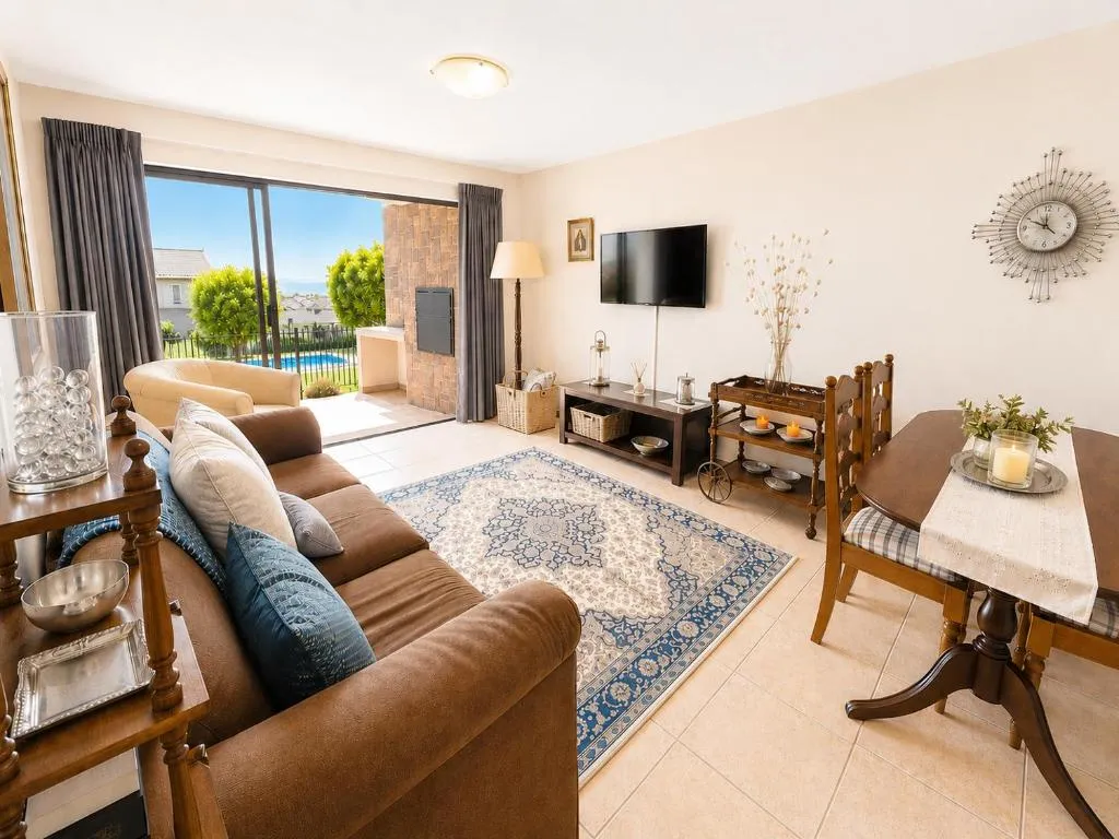 Living room with a brown sofa, patterned rug and sliding doors onto the pool terrace