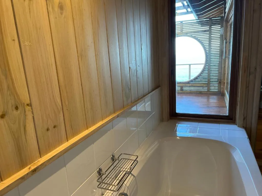Bathroom with freestanding tub and a round porthole window framing a sea view