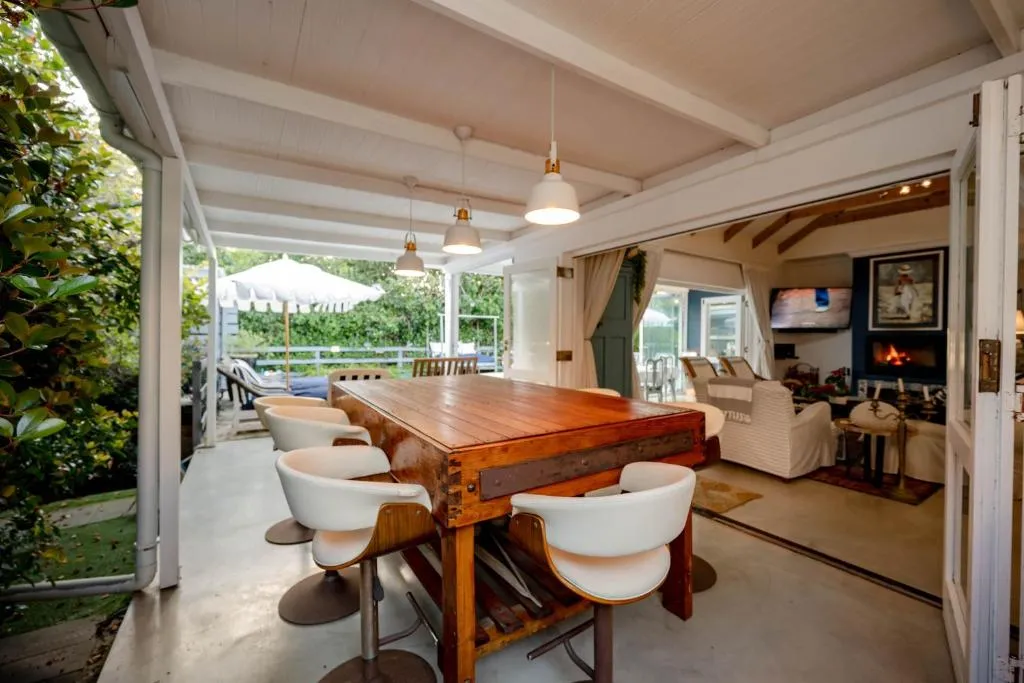 Covered outdoor dining table under pendant lights, opening onto the pool terrace and lounge