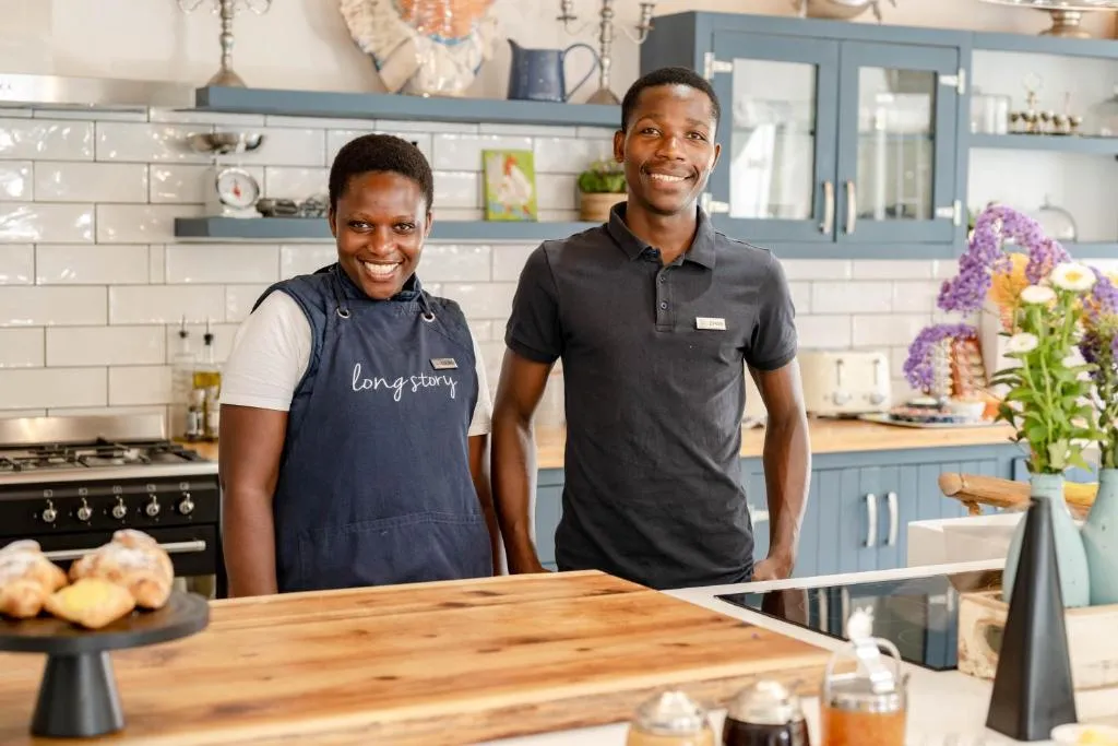 Guest house staff behind the kitchen counter, with blue cabinetry and subway tile behind