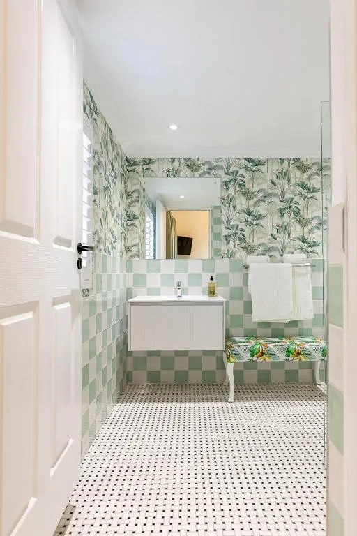 Bathroom with green checkerboard tile, palm-print wallpaper and a walk-in shower