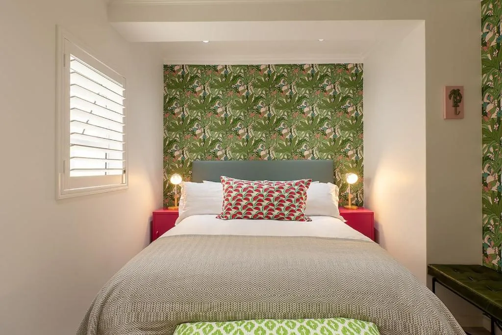 Bedroom with tropical leaf wallpaper, a teal headboard and twin bedside lamps