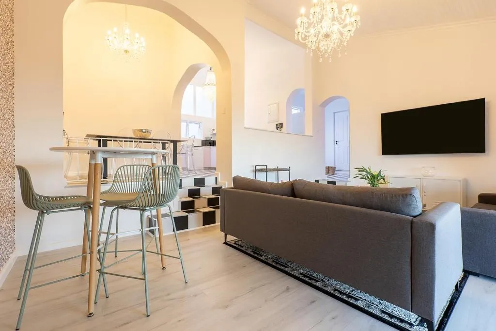 Lounge with a grey sofa, wall-mounted TV, chandelier and archways into the dining area