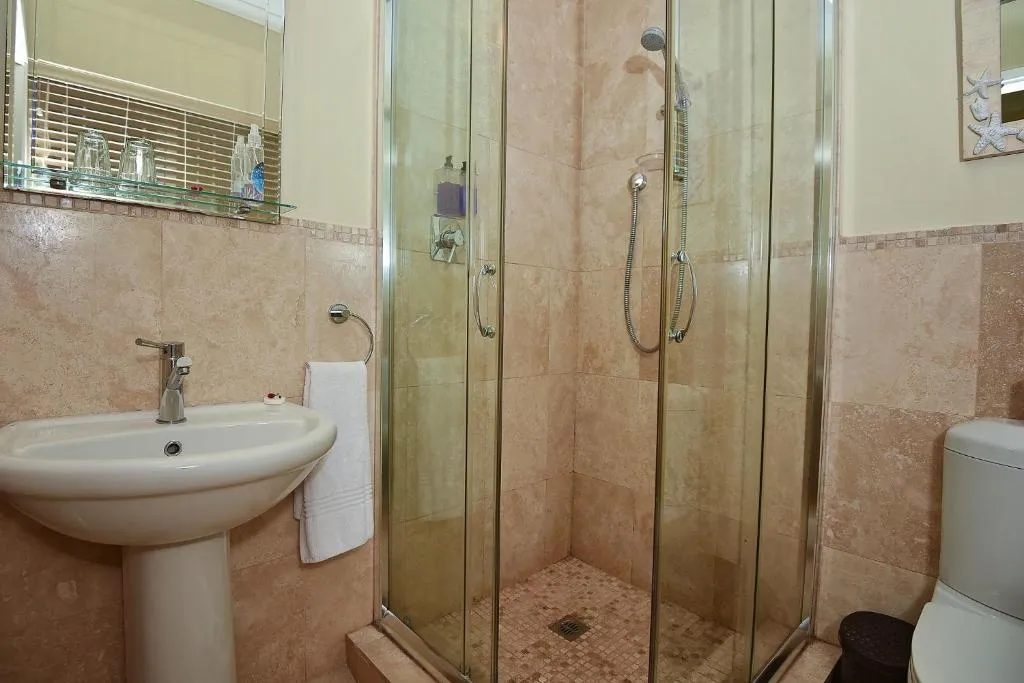 Bathroom with a corner glass shower and pedestal sink on travertine-style tiles