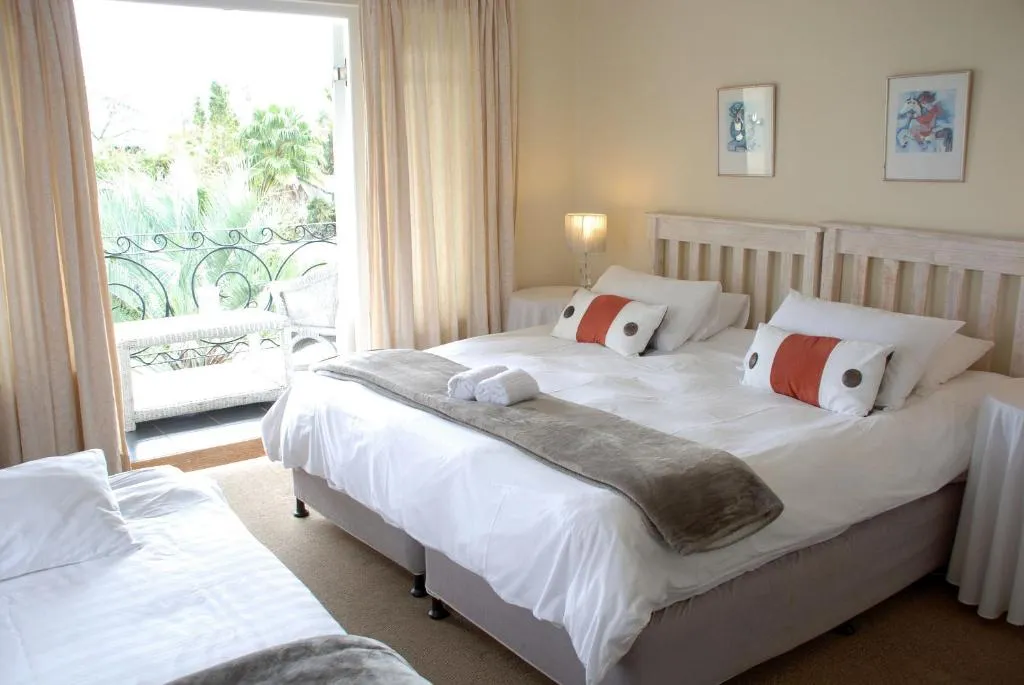 Twin bedroom with orange accent pillows and French doors onto a balcony over the garden