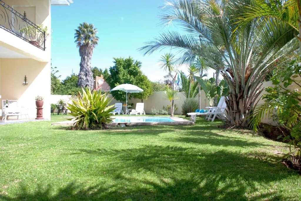 Garden lawn with a swimming pool, sun loungers, and a shaded umbrella table