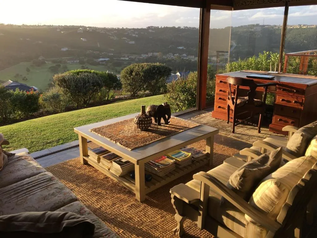 Covered patio seating area with wooden furniture overlooking rooftops and hills