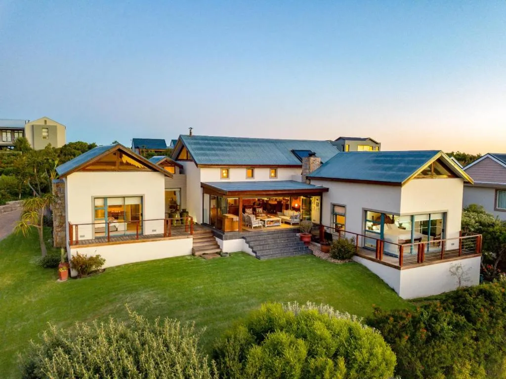 Twilight view of the gabled house with two wraparound timber decks lit from inside