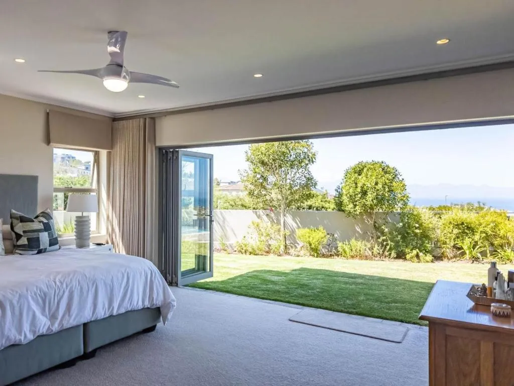 Bedroom with sliding doors open to a lawn, a glimpse of the sea visible beyond the garden wall