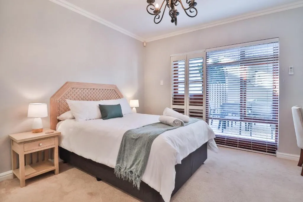 Bedroom with a wood-panelled headboard, bedside lamps, and plantation-shuttered doors