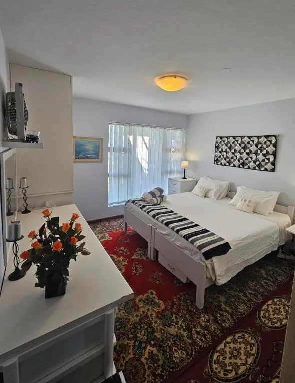 Bedroom with a white double bed, patterned red rug and sliding door to a window