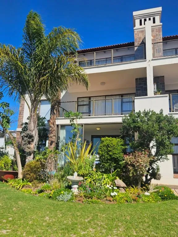 Double-storey house with balconies and stone chimney behind a lush palm and garden bed