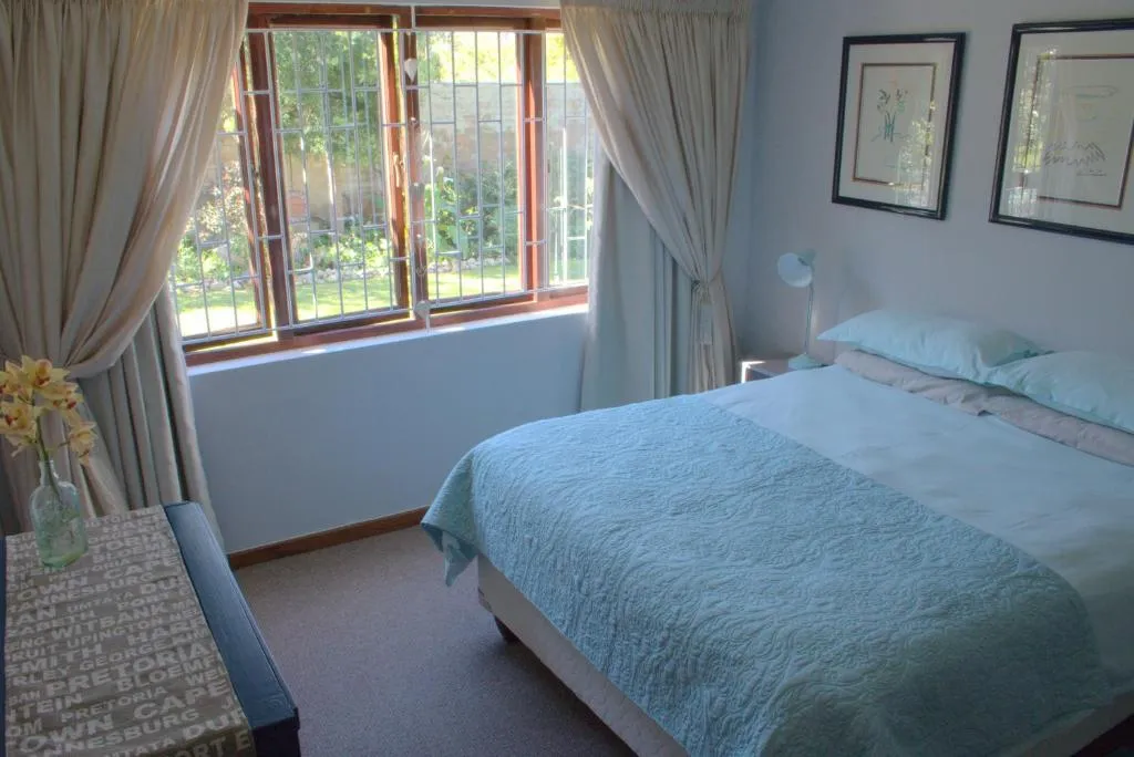 Bedroom with a pale quilted bedspread and a barred window looking onto the garden