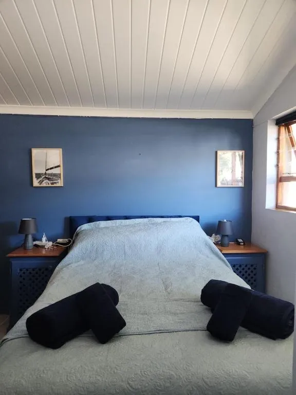 Bedroom with a navy feature wall, boat print artwork and bolster cushions on the bed