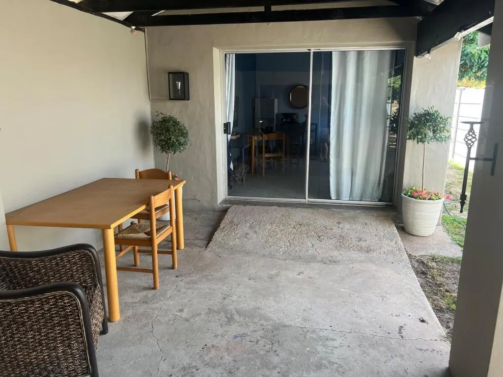 Covered outdoor dining patio with a wooden table and chairs, potted olive trees and sliding doors