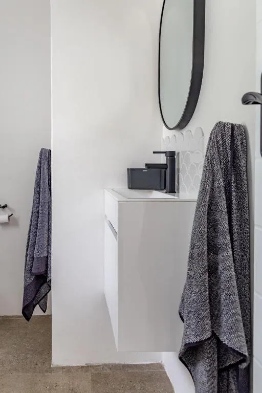 Bathroom vanity with a round mirror, black tapware and hanging towels