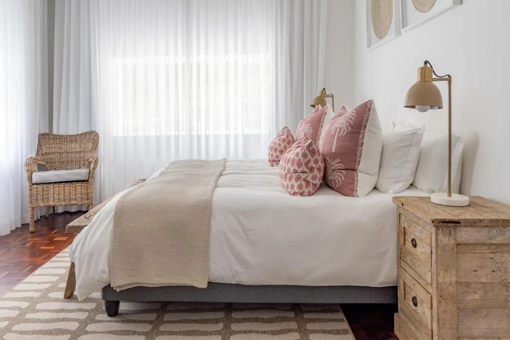 Bedroom with a wicker armchair, parquet floor and pink palm-print cushions