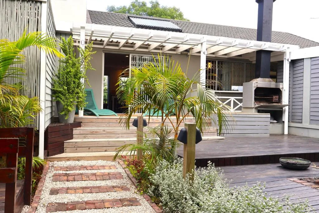 Covered deck with a built-in braai, pergola and solar panels above, teal loungers alongside