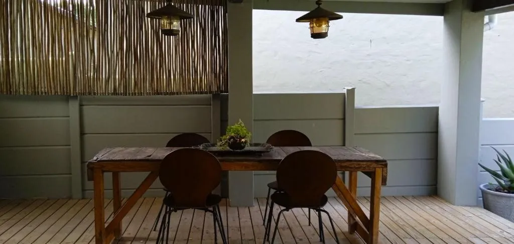 Outdoor dining table under a covered deck, screened by a bamboo wall with hanging lanterns