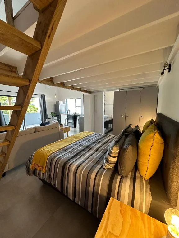 Loft-style bedroom beneath a wooden mezzanine with striped bedding and a window seating nook