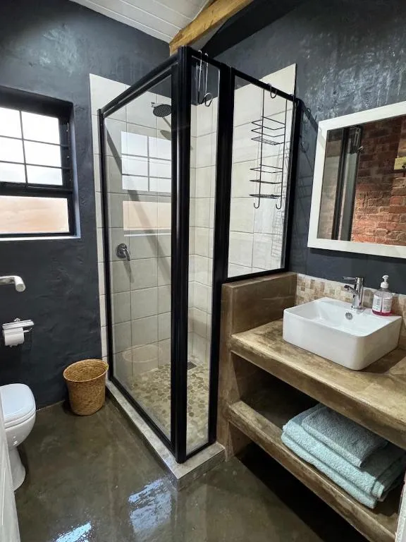 Bathroom with a corner glass shower, dark walls and a brick-tiled vanity