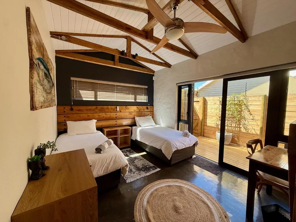 Twin bedroom with exposed wooden roof beams and glass doors onto a private deck