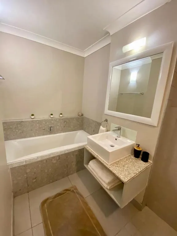Bathroom with a tiled bath, pedestal-style basin, and a large square mirror