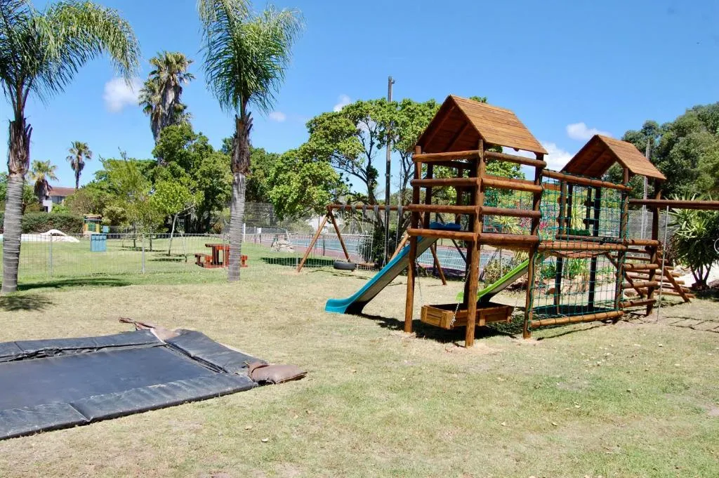 Estate playground with a wooden jungle gym, slide, and swings near the tennis court