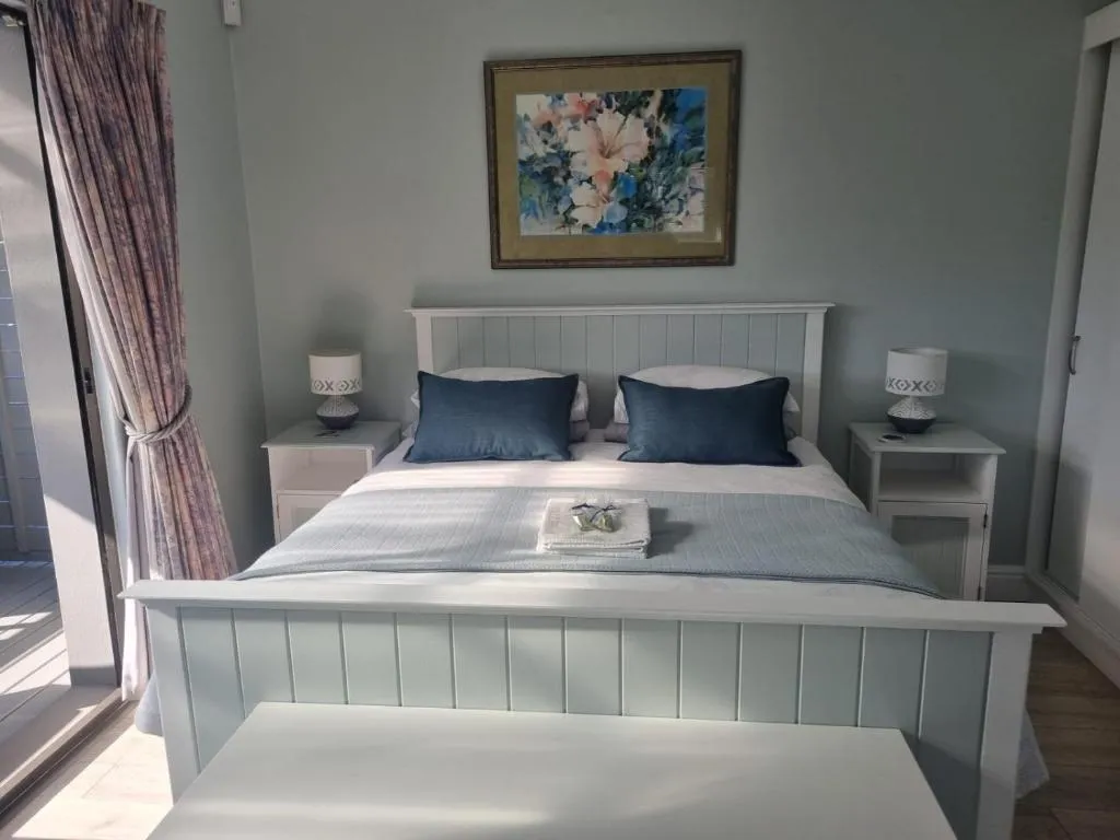 Bed with white panelled headboard, navy cushions and bedside table lamps