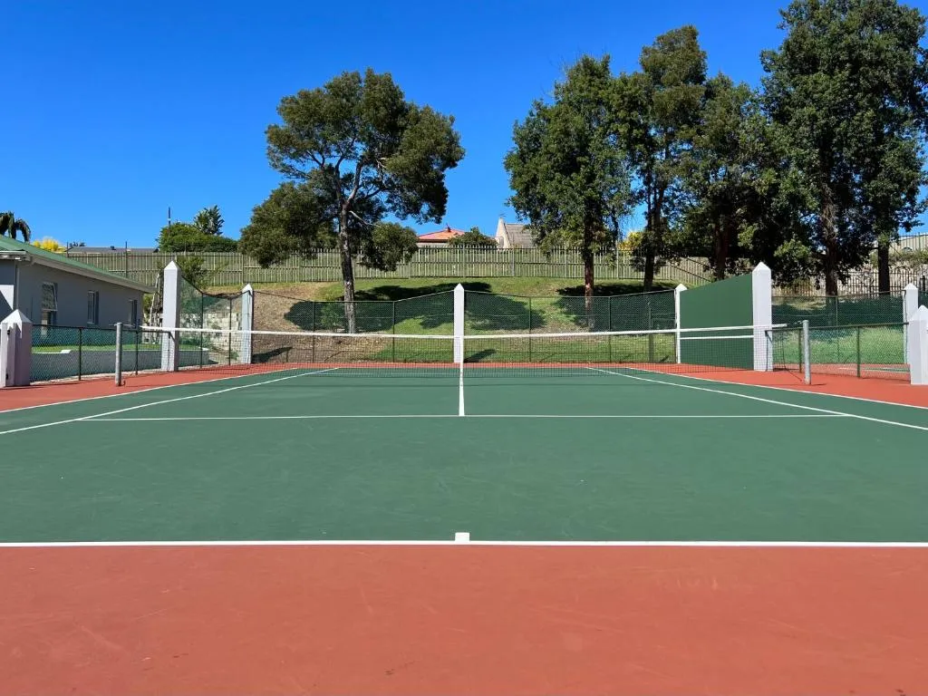 Shared estate tennis court bordered by trees and a green hillside fence