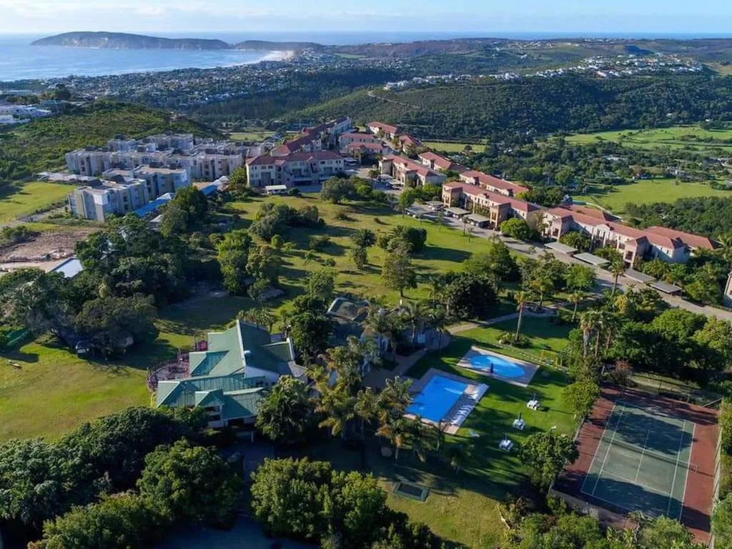 Aerial view of the estate showing pools, a tennis court and coastline beyond
