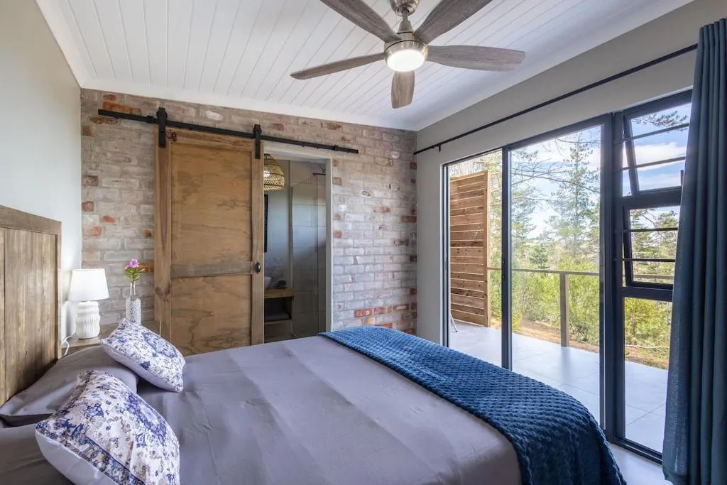 Bedroom with exposed brick, ceiling fan and sliding doors onto a forest-view deck