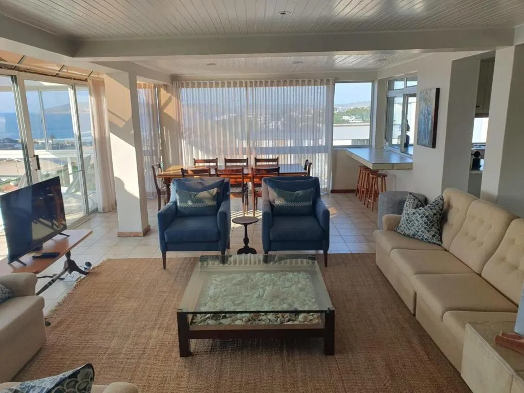 Open-plan living room with blue armchairs, sectional sofa and a sea view through the balcony doors