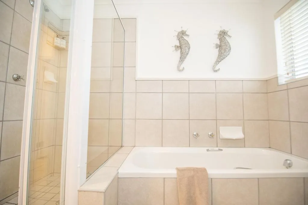 Bathroom with a corner bath, glass shower and seahorse wall art