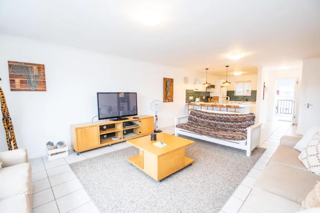 Living area with a striped futon, TV unit and open door onto the balcony