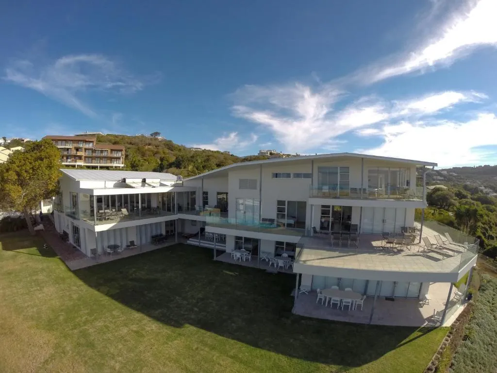 Aerial view of the villa's wraparound terraces, pool and lawn above the coastline