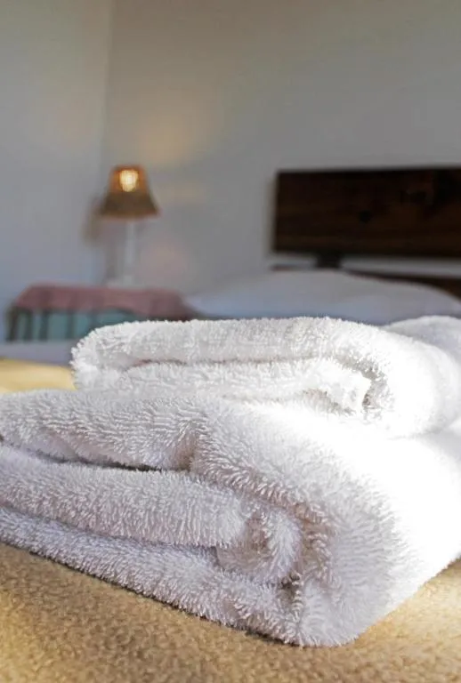 Folded towels on a bed with a lamp and headboard in the background