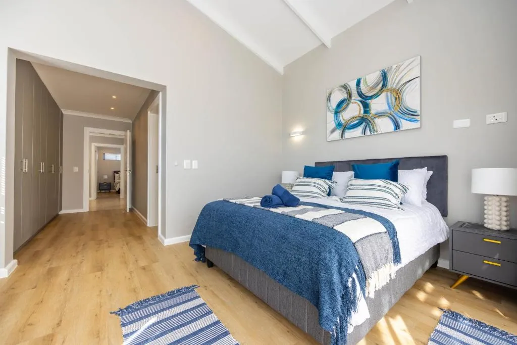 Bedroom with a grey upholstered bed, striped throws, and a walk-in wardrobe visible through the doorway