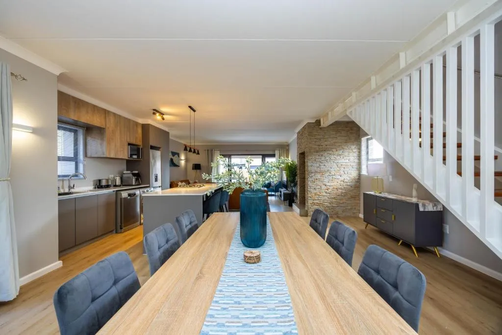 Long dining table seating eight, open to a wood-cabinetry kitchen with a dishwasher