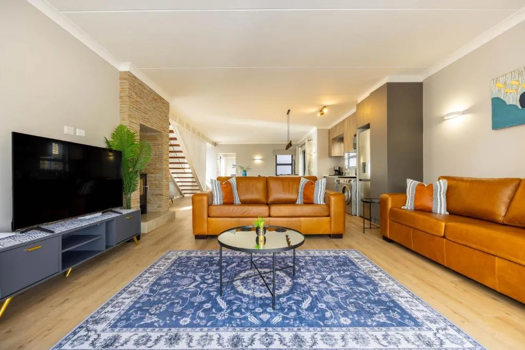 Living room with tan leather sofas, a stone-clad fireplace, and an open staircase to the upper level