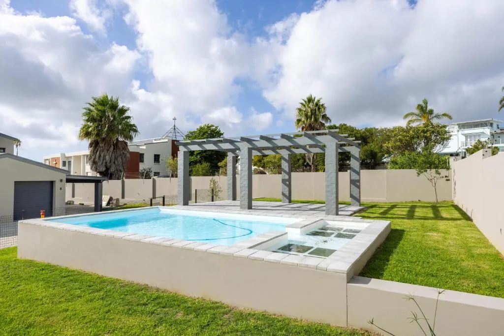 Private walled swimming pool with a paved surround, pergola, and lawned garden
