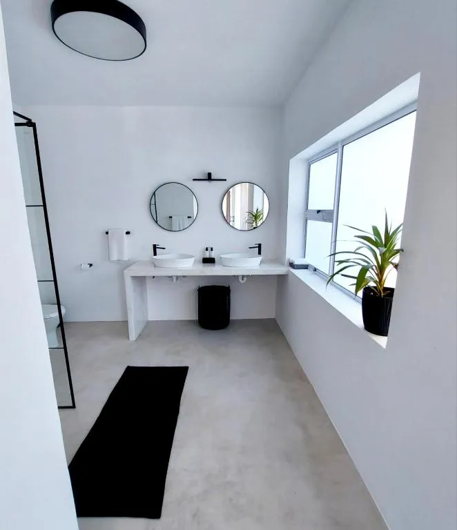 Bathroom with dual vessel sinks, round mirrors, a walk-in shower, and a large window