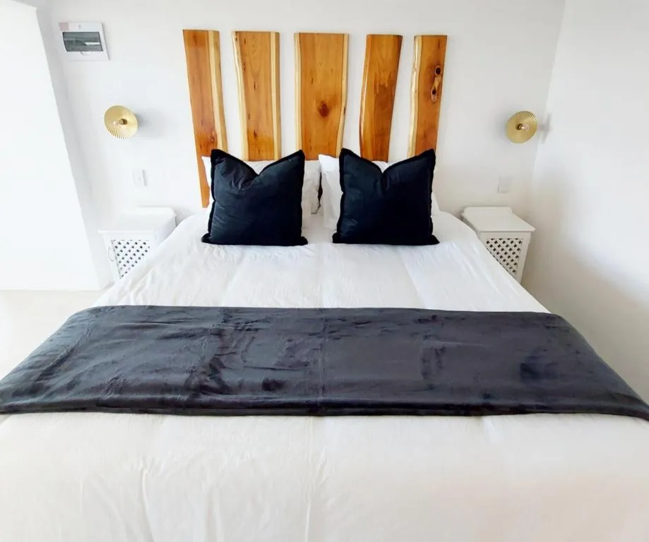 Bed dressed in white linen with a live-edge wood headboard and a charcoal throw