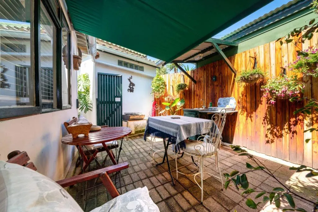 Covered courtyard patio with a wrought-iron dining set, small braai, and hanging flower baskets