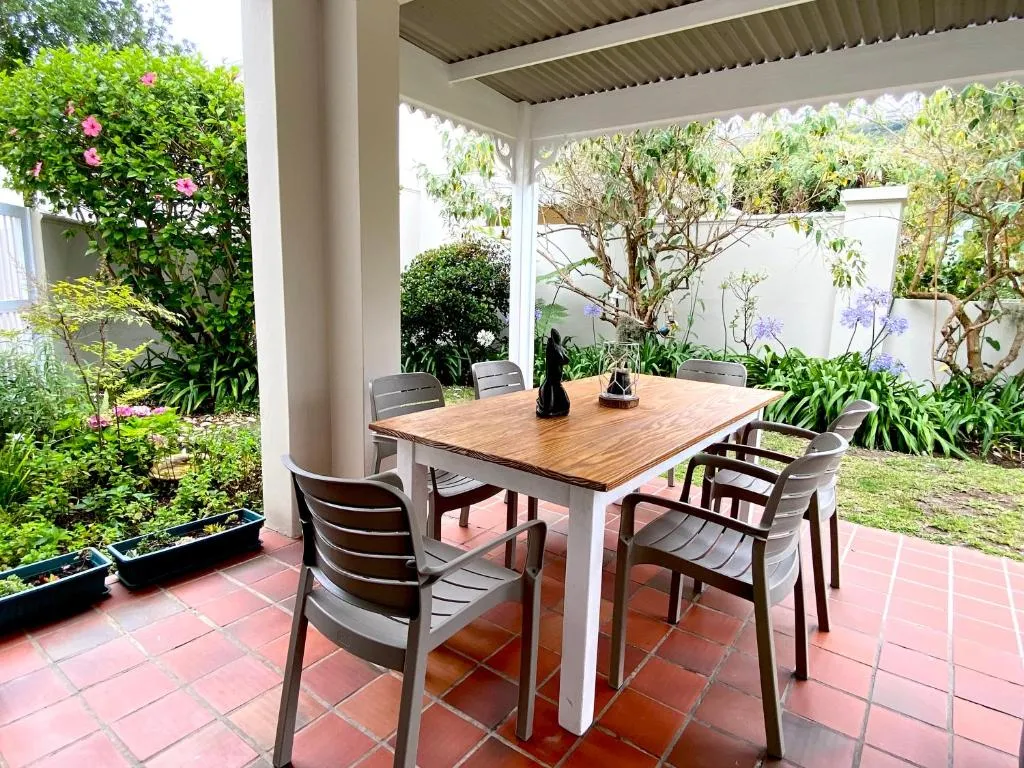 Covered patio with a wooden dining table for six, surrounded by garden shrubs and flowering agapanthus