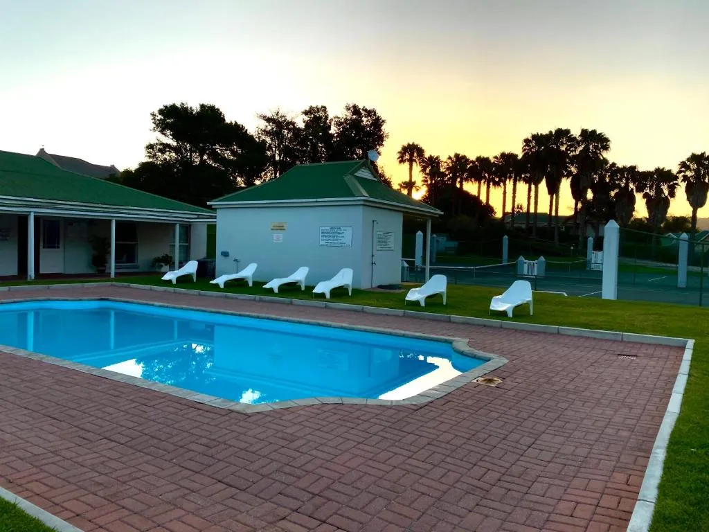 Shared estate pool and loungers beside the clubhouse at sunset, with tennis courts and palms beyond