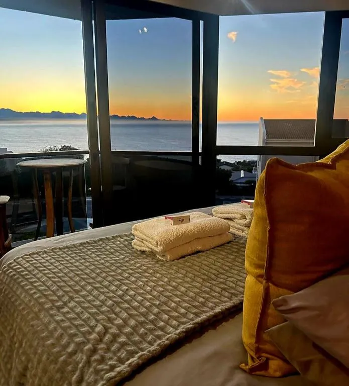 Bedroom with floor-to-ceiling windows framing an ocean sunset, folded towels on the bed