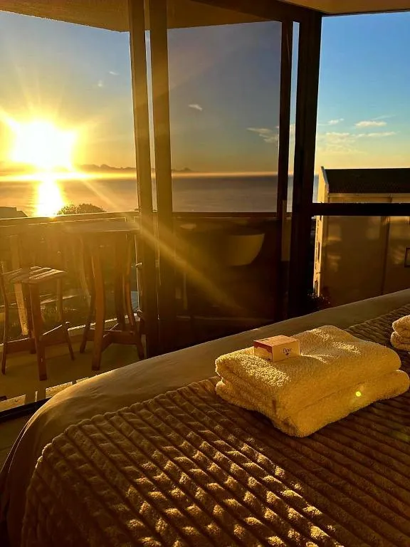 Sunrise over the sea seen through an open balcony door, with wooden bar stools outside